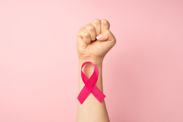 First person top view photo of raised female hand with clenched fist and pink ribbon on wrist...