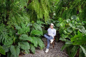 Handsome Asian man loves to plant trees sitting in a garden monstera is using his laptop computer...