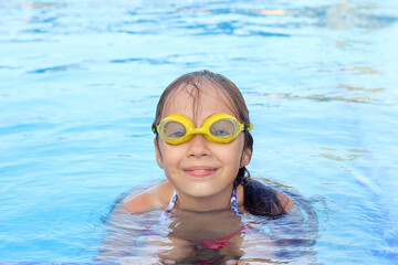 Naklejka premium Cute little girl is smiling in swimming pool. Summer, vacation, sport concept