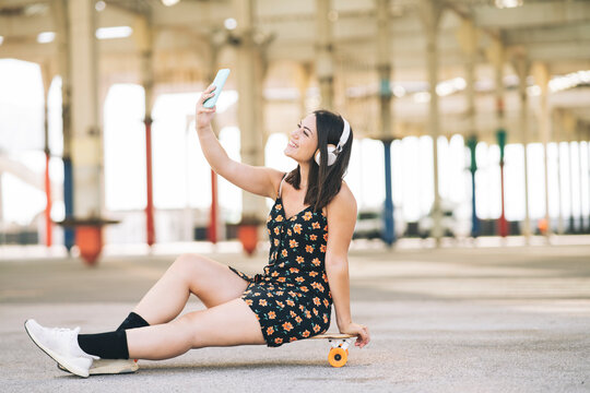 woman with smartphone headphones and skateboard, making selfie