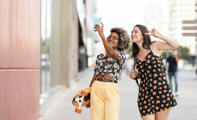 two multi-ethnic women strolling while taking photos with smartphone