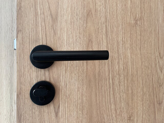 Closeup detail of door handle in house, wooden door with black handle set.