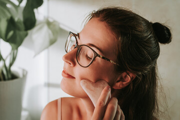 Woman in eyeglasses doing face lifting massage with gua sha in front of a mirror