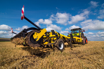 tractor with a heavy disc harrow on the field with cloudly sky