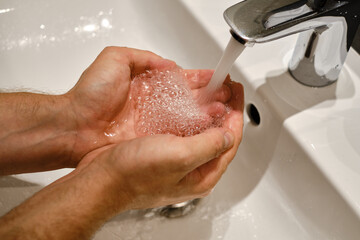 Fototapeta premium A man washes his hands with water in the bathroom. Human hands close up. Health concept. Keeping your hands clean is the best way to prevent the spread of infection