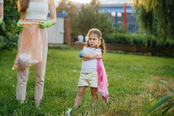 A little girl is upset about cleaning garbage in the park during sunset. Environmental care, recycling.