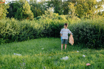 Naklejka na ściany i meble A seven-year-old boy at sunset is engaged in garbage collection in the park. Environmental care, recycling.