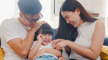 Happy cheerful Asian family dad, mom and daughter having fun cuddling playing on sofa while birthday at house. Self-isolation, stay at home, social distancing, quarantine for coronavirus prevention.