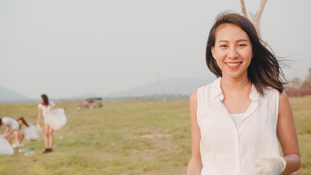 Portrait of young Asia lady volunteers help to keep nature clean up, looking at camera and smile with white garbage bags on the beach. Concept about environmental conservation pollution problems.