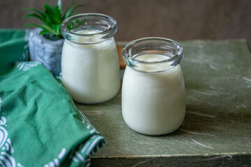 white yogurt in two glass jars on green background