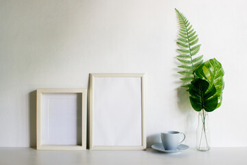 A frame with coffee and monstera leave on a white wall with nature light. 