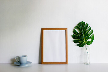 A frame with coffee and monstera leave on a white wall with nature light. 