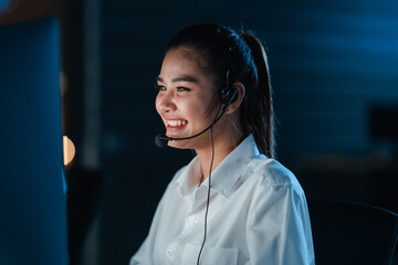 Millennial Asia young call center team or customer support service executive using computer and microphone headset working technical support in late night office. Telemarketing or sales job concept.
