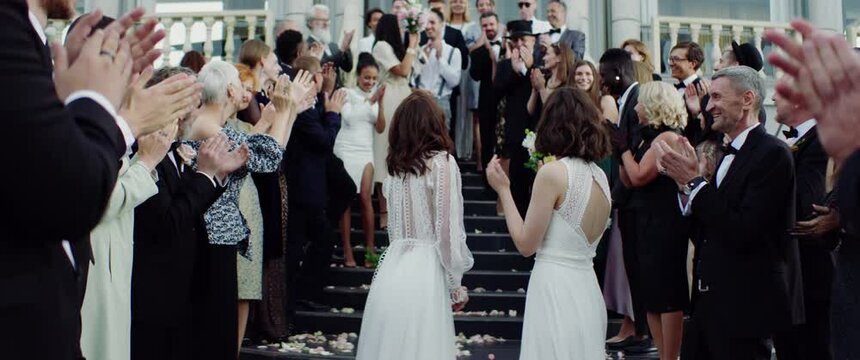 Candid shot of two female lesbian LGBT brides toss their bouquets over their shoulders to their guests. Shot with 2x anamorphic lens