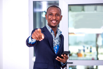 young businessman holding mobile phone and pointing finger at you while smiling.