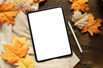 close up top view white  blank digital tablet screen and stylus pen with group of dried orange color maple leaves on wood background texture or autumn season collection design concept