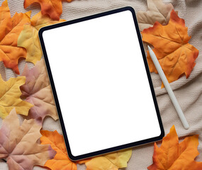 close up top view white blank digital tablet screen and stylus pen with group of dried orange color maple leaves on sweater fabric background texture or autumn season collection design concept	