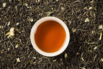 a cup of jasmine scented tea on dried tea leaves background