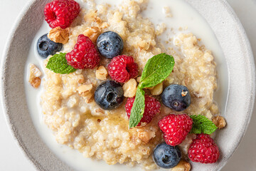 Quinoa porridge with fresh berries, nuts, honey and mint in a bowl on white background. top view. close up. healthy breakfast