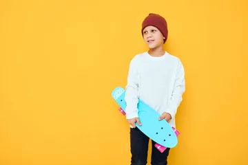 Tuinposter Cool smiling boy in a red hat skateboard in his hands yellow color background © SHOTPRIME STUDIO