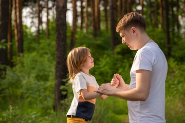 Caucasian girl of 6 years holding dad's hand looking at each other in forest.