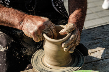 Hands of a potter shaping a clay pot on a potter wheel