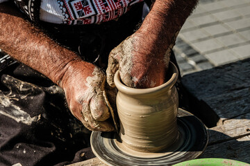 Hands of a potter shaping a clay pot on a potter wheel