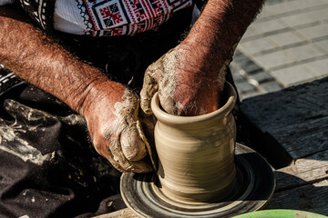 Hands of a potter shaping a clay pot on a potter wheel