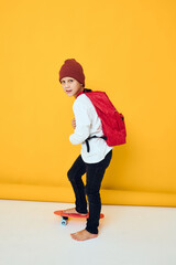 Fototapeta na wymiar a schoolboy stands on a skateboard on a yellow background