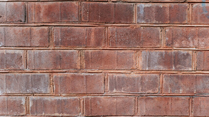 Wall of dark red rough brick close-up, textured background outside of the building outdoors, horizontal brickwork