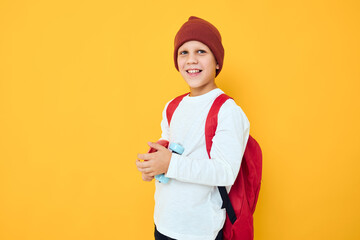 Cheerful little kid with red backpack red skateboard yellow color background