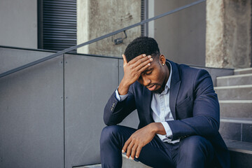 african businessman sitting frustrated on the stairs depressed by the results of his work, holding hands behind his head
