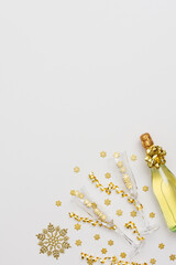 Festive white background with gold decoration , bottle of sparkling wine with two crystal glasses, shiny golden serpentine confetti and glittering snowflakes, copy space, top view