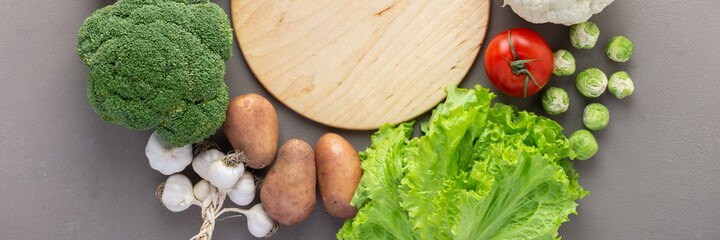 Fresh farm organic vegetables banner, healthy food concept, vegetables and mushrooms around a round cutting board on a gray background, top view, copy space