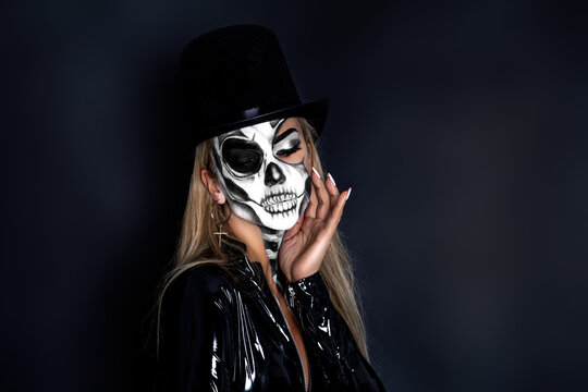 Beautiful model in Halloween makeup on black background. Sexy woman in top hat and skull makeup. Halloween makeup concept.