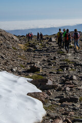 group of hikers with a patch of snow in the foreground and a sea of low clouds in the background