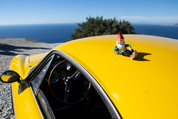 porcelain gnome lying on the hood of a yellow car with the sea in the background