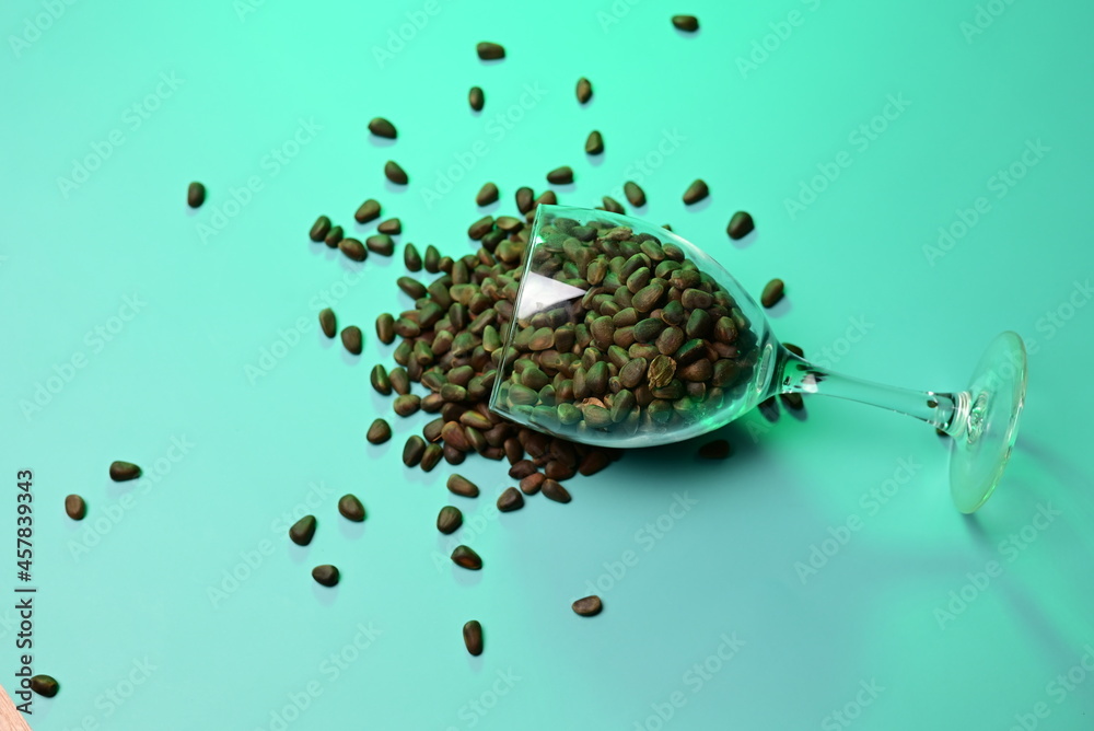 Wall mural sprinkled pine nuts in a transparent glass on a green background