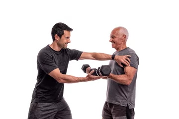 Foto auf Leinwand An elderly European man, with a personal trainer, trains, lifting weights, on a white background. © sergojpg
