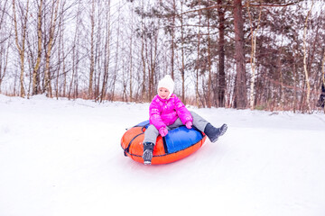 A cheerful girl in warm clothes rides down snowy hill on slide-slide cheesecake