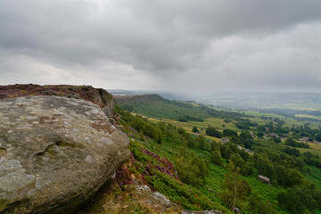 On a summer morning unseasonably dark grey skies and mist over Curbar Edge the Derbyshire Peak District.