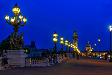 Pont Alexandre III bridge over river Seine and Hotel des Invalides on background at night in Paris, France.  Cityscape of Paris. Architecture and landmarks of Paris.