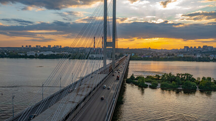 South bridge in Kiev. Sunset over the Dnieper. Thick clouds over the evening city. Evening shot of the bridge. Orange sun at sunset. The rays break through the clouds and are reflected in the river.