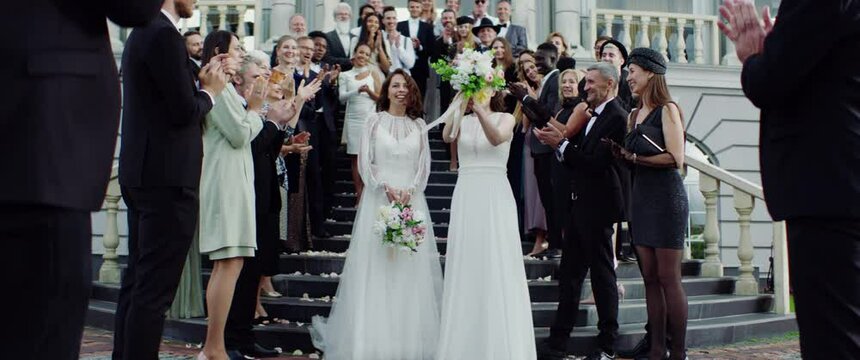 Candid shot of two female lesbian LGBT brides toss their bouquets over their shoulders to their guests. Shot with 2x anamorphic lens