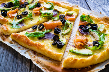 Pizza with smoked salmon, arugula, avocado, mozzarella and black olives on wooden background
