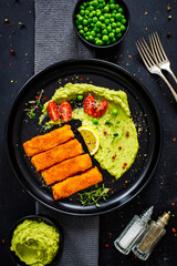 Fried fish sticks with potato and peas puree on wooden black table
