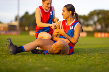 women in football uniform sitting on ground with strapping tape