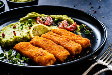 Fried fish sticks with potato and peas puree on wooden black table
