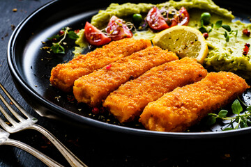 Fried fish sticks with potato and peas puree on wooden black table
