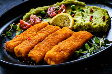Fried fish sticks with potato and peas puree on wooden black table
